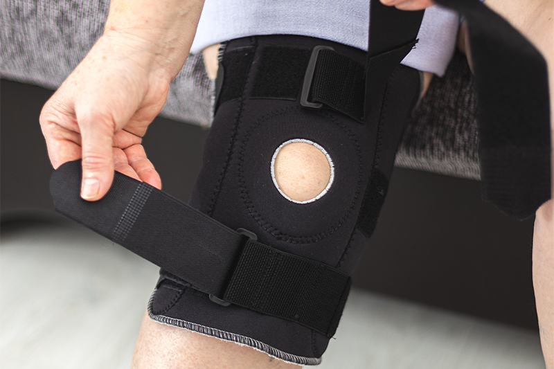 Person who puts on protective knee brace, knee support at home